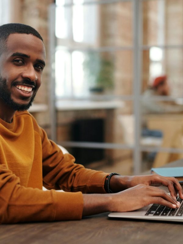 African American man typing on laptop in cozy modern office setting, smiling and focused.