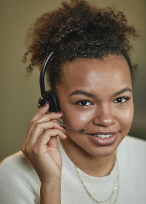 Close-up of a smiling woman with afro hair wearing a headset, providing customer support.